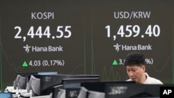 A currency trader watches monitors near a screen showing the Korea Composite Stock Price Index, left, and the foreign exchange rate between the U.S. dollar and the South Korean won at KEB Hana Bank headquarters in Seoul, South Korea, Dec. 26, 2024.