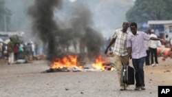 Deux hommes portant une valise, dépassent une barricade de feu à Bujumbura, Burundi, le 30 avril 2015.