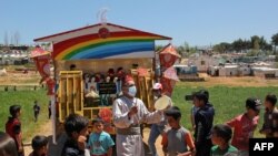 Anak-anak berkumpul di sekitar aktor tunggal yang tampil untuk menghibur anak-anak di kamp pengungsi Suriah, di kota selatan Lebanon Ebel al-Saqi di bulan Ramadan, 23 April 2021. (Foto: Ali DIA / AFP)