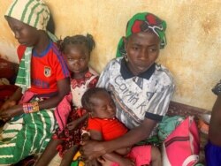 FILE - A woman who fled the violent rebellion in Central African Republic (CAR), sits with her family as they wait for their identification process in the border town of Garoua Boulai, Cameroon, Jan. 7, 2021.