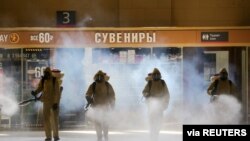 FILE - Russia's Emergencies Ministry members wearing personal protective equipment spray disinfectant near a gift kiosk at the Kievsky Railway Station in Moscow, May 18, 2020. 