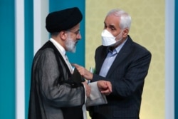 In this picture made available by the Young Journalists Club, presidential candidates Mohsen Mehralizadeh, right, and Ebrahim Raisi talk on the sidelines of the final candidates debate at a state-run TV studio in Tehran, Iran, June 12, 2021.