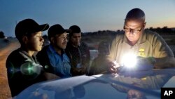 FILE - A U.S. Customs and Border Patrol agent gathers information on four Guatemalan nationals, July 18, 2018, in Yuma, Ariz. 