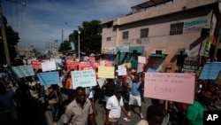 FILE - Several hundred protesters march carrying signs in Creole calling for President Jovenel Moïse to resign, in Port-au-Prince, Haiti, Oct. 21, 2019.