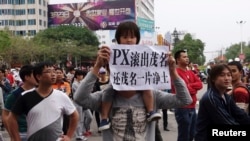 A man carrying a girl on his shoulder holds up a paper reading "PX (paraxylene petrochemicals) get out of Maoming, return us clean land", as demonstrators gather to protest against a chemical plant project, near the city government building in Maoming, Gu