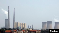 The cooling towers and chimneys from a coal-burning power station can be seen behind a man standing next to his car in a newly constructed residential area in Beijing, (File photo).