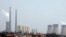 The cooling towers and chimneys from a coal-burning power station can be seen behind a man standing next to his car in a newly constructed residential area in Beijing, (File photo).