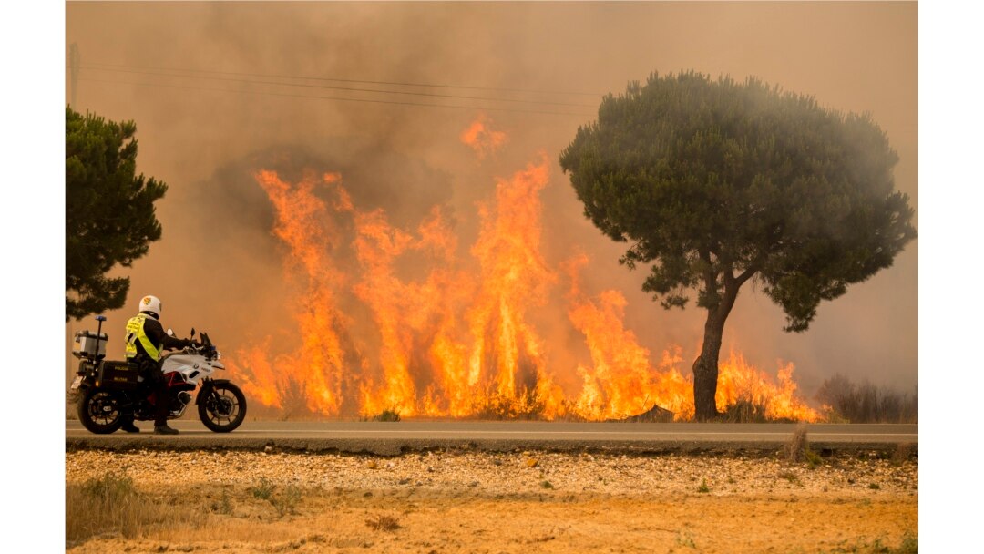 FILE - A military police officer stands by his motorcycle next to flames from a forest fire near Mazagon in southern Spain, June 25, 2017.
