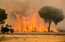 FILE - A military police officer stands by his motorcycle next to flames from a forest fire near Mazagon in southern Spain, June 25, 2017.
