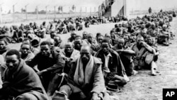 FILE - Some of the many Kikuyu tribesmen who were detained as Mau Mau suspects after the forced evacuation of Kikuyus accused of squatting on European farms in the Thomson's Falls area, Kenya, wait to be transported on Nov. 30, 1952. The enclosure is surrounded by barbed wire.