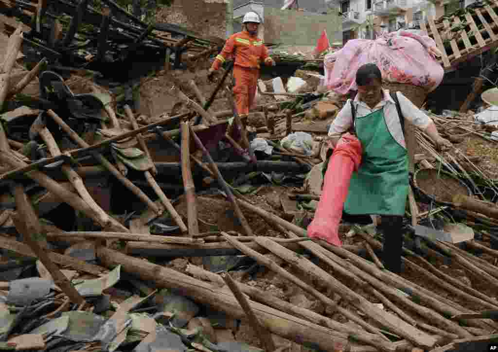 A villager carries her belongings and walks through the rubbles from destroyed houses following a massive earthquake in the town of Longtoushan in Ludian County, Aug. 5, 2014.