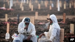 Workers take a break during a busy day at Rorotan Cemetery, which is reserved for those who died of COVID-19, in Jakarta, Indonesia, July 1, 2021.