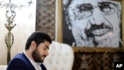 In this Sept. 30, 2018 photo, Abdullah Morsi, the youngest son of Egypt’s jailed former Islamist President Mohamed Morsi, sits in front of a framed image of his father. (AP Photo/Brian Rohan)
