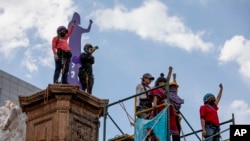 Mujeres levantan los brazos después de colocar una escultura sobre un monumento dedicado a los derechos de las mujeres titulado "Glorieta de las mujeres que luchan" antes del Día Internacional de la Mujer, en Ciudad de México, sábado, 5 de marzo de 2022.