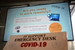 FILE - A screen promoting remote working using a laptop or a mobile phone to promote the fight against COVID-19 is displayed at the World Health Organization headquarters in Geneva, March 11, 2020.