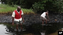 FILE- In this June. 20, 2010 file photo, men walk in an oil slick covering a creek near Bodo City in the oil-rich Niger Delta region of Nigeria.