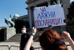 A protester holds a banner reading: ''Boo. Phoney Lawmakers!'', during a protest in front of parliament building before the inaugural parliament session in Belgrade, Serbia, Aug. 3, 2020.