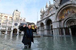 A man carries suitcases as he wades through water during a high tide of 1.44 meters (4.72 feet), in St. Mark's Square, in Venice, Italy, Dec. 23, 2019.