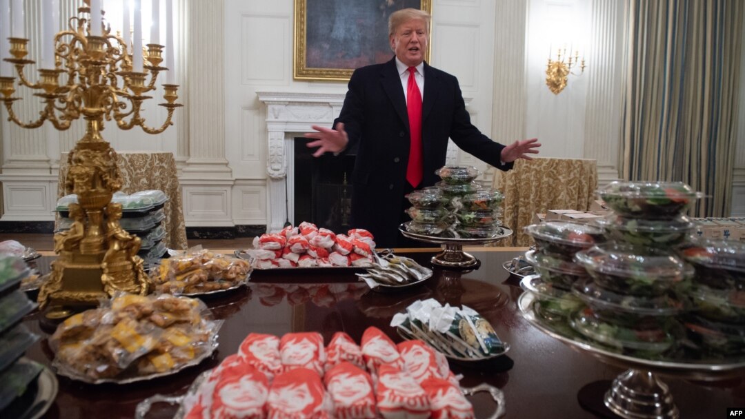 Presiden AS Donald Trump sedang berbicara di belakang meja yang berisi makanan cepat saji yang dibelinya untuk menjamu Juara Nasional Sepak Bola AS Liga Perguruan Tinggi 2018, Clemson Tigers, di Ruang Jamuan Kenegaraan di Gedung Putih, Washington DC, 14 Januari 2019

