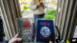 FILE - A woman holds copies of "The Satanic Bible" by Church of Satan founder Anton Szandor LaVey and "The Bible of the Adversary" by Michael Ford, before the start of a ceremony at the General Cemetery in Santiago, Chile, Sept. 14, 2024.