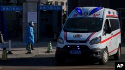 An ambulance passes a worker in protective gear outside a fever clinic in Beijing, Dec. 19, 2022.