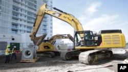 FILE - An excavator prepares to lift a storm water drainage pump on a construction site in Miami Beach, Florida.