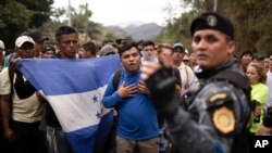 Migrantes hondureños, enarbolando la bandera de su país, se detienen ante policías guatemaltecos cerca de Agua Caliente, Guatemala, el 16 de enero de 2020.