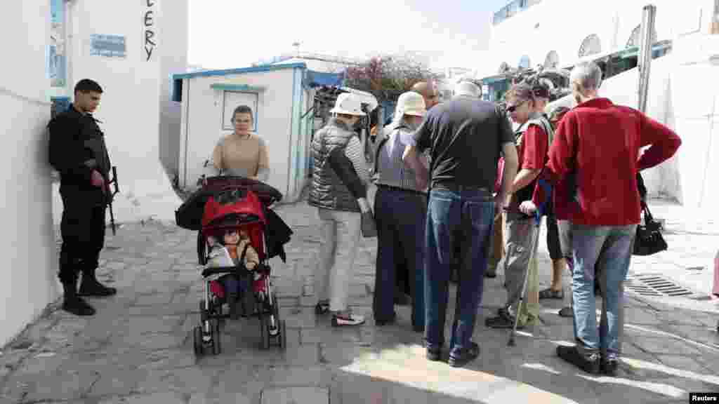 Un officier de police débout, monte la garde pendant que des touristes se promènent à Sidi Bou Said, une destination touristique, à Tunis, lundi 23 mars 2015.