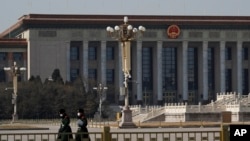 FILE - Paramilitary policemen wearing protective face masks are seen walking in an empty Tiananmen Square against the backdrop of the Great Hall of the People in Beijing, China, Feb. 23, 2020.