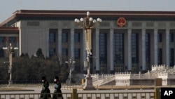 FILE - Paramilitary policemen wearing protective face masks walk by the empty Tiananmen Square against the back drop of the Great Hall of the People in Beijing, Feb. 23, 2020.