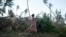 A woman carrying her baby walks past fallen trees in Tanna, Vanuatu, where residents told relief workers they were running low on food and other basic supplies, March 18, 2015. 