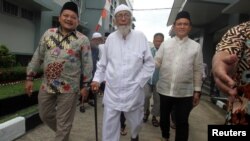 Abu Bakar Ba'asyir (tengah), tersangka dalang Bom Bali 2002 berjalan bersama Yusril Ihza Mahendra (kanan), penasihat pasangan capres-cawapres Joko Widodo-Ma'ruf Amin, di Lapas Gunung Sindur di Bogor, Indonesia, 18 Januari 2019.