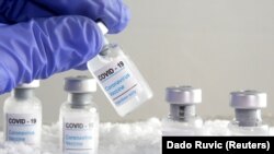 Woman holds a vial labeled "COVID-19 Coronavirus Vaccine" over dry ice in this illustration taken, December 5, 2020.