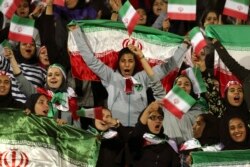 FILE - Iranian women cheer as they wave their country's flag after authorities in a rare move allowed a select group of women into Azadi stadium to watch a friendly soccer match between Iran and Bolivia, in Tehran, Oct. 16, 2018.