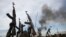 FILE - Rebel fighters hold up their rifles as they walk in front of a bushfire in a rebel-controlled territory in Upper Nile state, South Sudan, Feb. 13, 2014. 