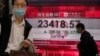 A man wearing a face mask walks past a bank's electronic board showing the Hong Kong share index at Hong Kong Stock Exchange Wednesday, March 25, 2020. Shares have advanced in Asia after the Dow Jones Industrial Average surged to its best day since 1933 a