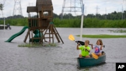 Siblings Avery, 10, and Grace LeBlanc, 7, canoe in their backyard next to playground equipment after flooding from Hurricane Francine in Montz, Louisiana, Sept. 12, 2024.