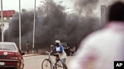 De la fumée s'élève alors que les militaires burkinabè, à l'arrière, néttoient les débris laissés par les manifestants sur une rue de Ouagadougou, au Burkina Faso, 18 septembre 2015.