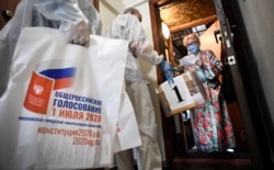 A woman wearing a protective mask stands by the door of her apartment as she prepares to cast her ballot in a mobile ballot box during a nationwide vote on constitutional reforms in Moscow, Russia, July 1, 2020.