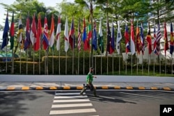 Seorang tukang kebun berjalan melewati bendera negara peserta di tempat penyelenggaraan Pertemuan Menteri Luar Negeri ASEAN dan Pertemuan Terkait di Jakarta, Selasa, 11 Juli 2023. (Foto: AP/Dita Alangkara)