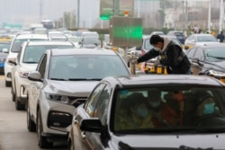 A staff member from a local sanitation and epidemic prevention team checks body temperature of a passenger in a car at a toll station in Wuhan, Hubei province, China Jan. 23, 2020.