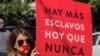 Una mujer sostiene un cartel que reza "Hay más esclavos ahora que nunca" mientras se une a cientos con camisas negras y cinta roja en la boca durante la tercera edición anual de la 'Caminata por la libertad' contra la esclavitud moderna, en México.