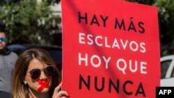 Una mujer sostiene un cartel que reza "Hay más esclavos ahora que nunca" mientras se une a cientos con camisas negras y cinta roja en la boca durante la tercera edición anual de la 'Caminata por la libertad' contra la esclavitud moderna, en México.