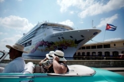 FILE - Tourists ride inside a vintage car as they pass by the Norwegian Sky cruise ship, operated by Norwegian Cruise Lines in Havana, Cuba, May 7, 2019.