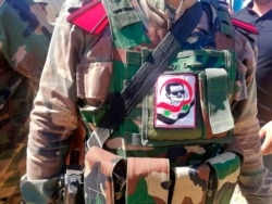 A Syrian soldier, with a picture of Syrian President Bashar Assad on his military uniform, organizes crowds during the opening ceremony of the crossing between the Iraqi and Syria, Sept. 30, 2019.