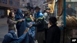 A man distributes bread to Burka-wearing Afghan women outside a bakery in Kabul, Afghanistan, Dec, 2, 2021.