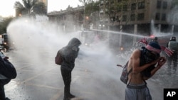Police spray anti-government protesters with water during a demonstration against police after an officer was accused of allegedly pushing a youth off a bridge during a previous protest in Santiago, Chile, Oct. 9, 2020. 