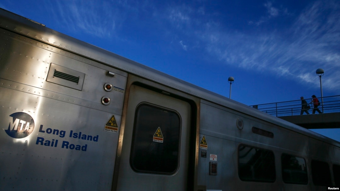 FILE - A Long Island Railroad train is seen parked as commuters make their way over a foot bridge in Port Washington, New York.