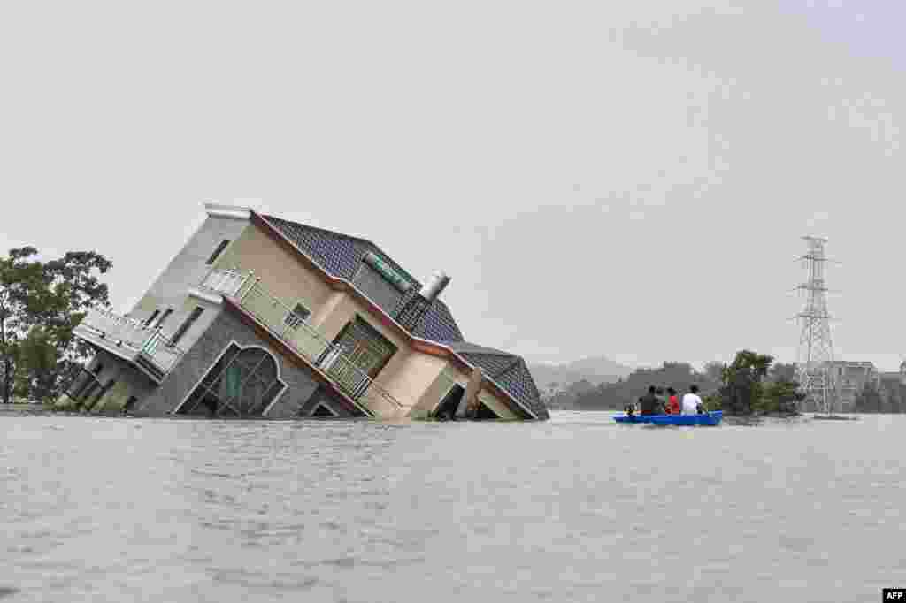 Residents ride a boat past a house damaged by torrential rains near the Poyang Lake in Poyang county, Shangrao city in China&#39;s central Jiangxi province, July 15, 2020.