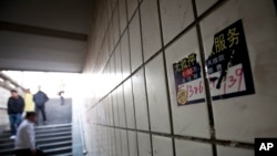 FILE - Pedestrian pass a partially torn advertisement leaflet of a private money lender displayed at an underground walkway in Beijing, China, Feb. 20, 2012.